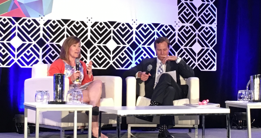 Two people sitting on stage in a panel discussion at a conference.